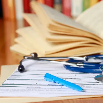 © shefkate - stock.adobe.com Ein Bild von einem Stethoskop, Büchern, Formularen und Stift