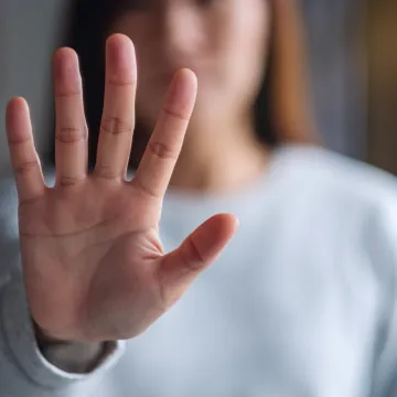 Eine Frau hält eine flache Hand mit den Fingern nach oben Richtung Kamera, um STOPP auszudrücken