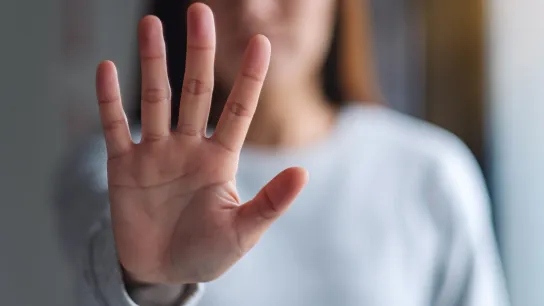 Eine Frau hält eine flache Hand mit den Fingern nach oben Richtung Kamera, um STOPP auszudrücken